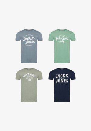 Mężczyzna w miętowozielonej koszulce Jack & Jones z białym napisem i niebieskich dżinsach, stojący z jedną ręką w kieszeni na białym tle.