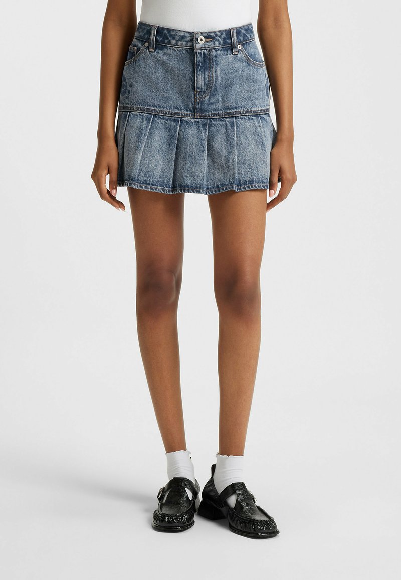 Jeansrok met een lichtblauwe wassing, voorzien van een aansluitende taille, uitlopende geplooide vorm en zichtbare stiksels. Afgewerkt met twee voorzakken.