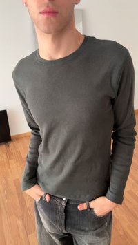 Camisola de manga comprida verde escura com nervuras, feita de tecido elástico, combinada com jeans pretos com textura desbotada.