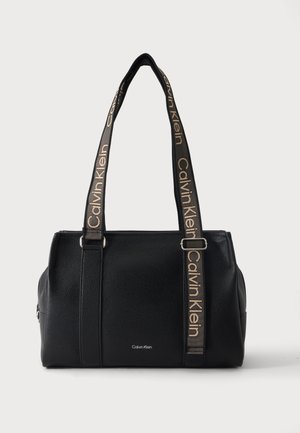 Sort Calvin Klein-håndtaske med tekstureret overflade og lang justerbar rem, med Calvin Klein-logo i beige på sort.