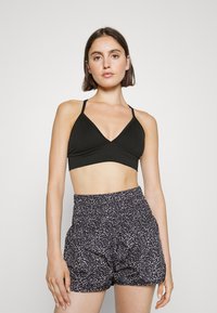 Bralette preta com nervuras, design em V e alças finas, combinado com calções de cintura alta com um padrão floral escuro.