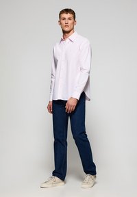 Lichtroze langarm overhemd met knopen en kraag, gecombineerd met donkerblauwe jeans en crèmekleurige sneakers. Rechte pasvorm en soepele textuur.