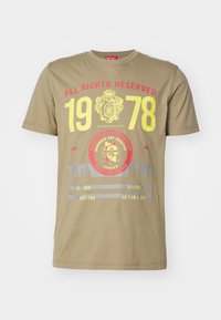 Khaki bavlněné tričko s krátkým rukávem, které má výrazné grafiky v červené a žluté barvě, včetně roku "1978" a různých tištěných vzorů.