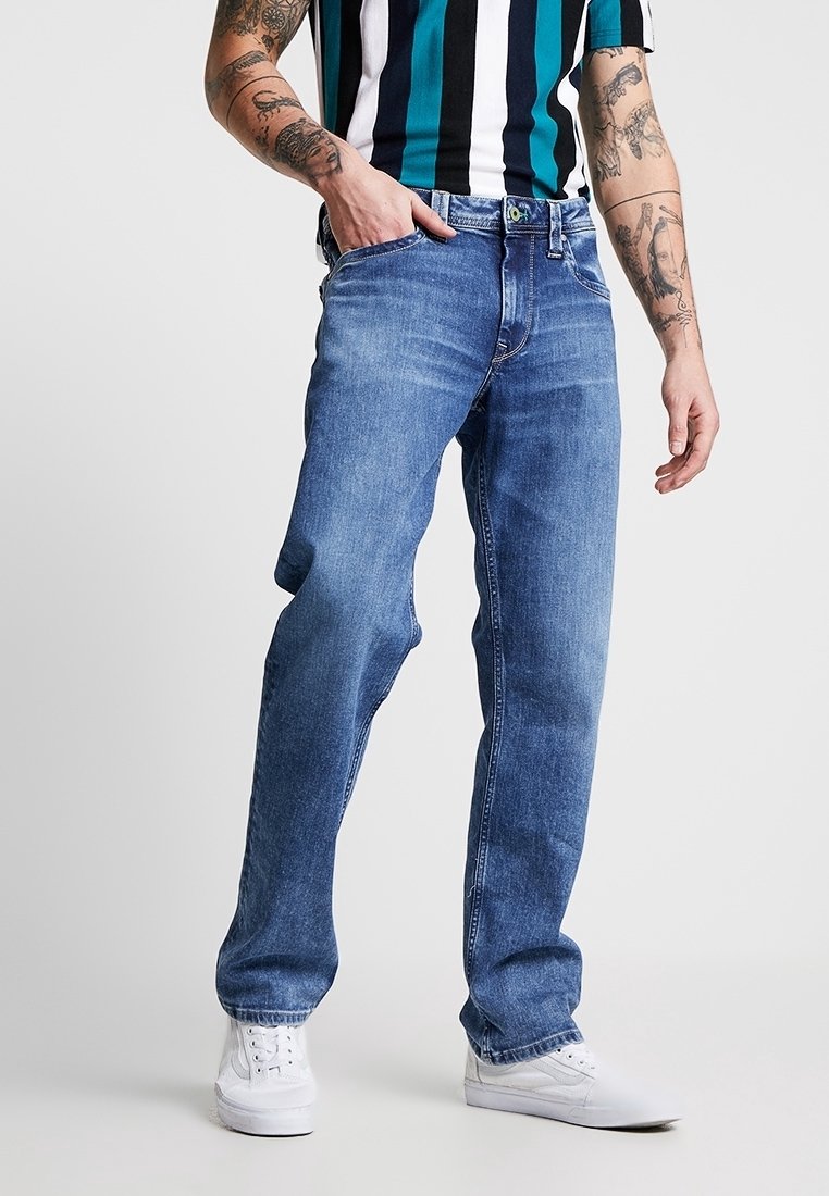 Vaqueros azules de denim con un ajuste relajado, con pierna recta, diseño clásico de cinco bolsillos y un sutil desgaste, combinados con zapatillas blancas.