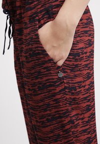 Czerwono-granatowe spodnie w wzory wykonane z miękkiego materiału, z bocznymi kieszeniami i ozdobnym guzikiem przy otworze kieszeni.