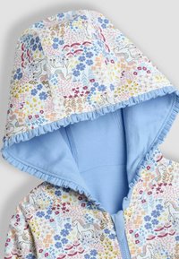 Chaqueta con capucha y forro azul, que presenta un patrón floral y unicornios blancos con acentos en colores pastel, y con un borde rizado alrededor del borde de la capucha.
