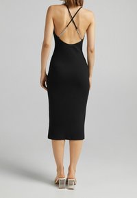 Robe midi noire côtelée avec un dos ouvert, ornée de bretelles entrecroisées et d'accents en chaîne métallique. Texture lisse, silhouette ajustée.