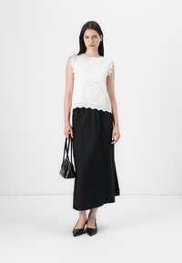 Fehér broderie anglaise top, fodros ujjakkal, hosszú fekete szoknyával párosítva. Kiegészítők között szerepel egy kis fekete táska és hegyes orrú lapos cipő.