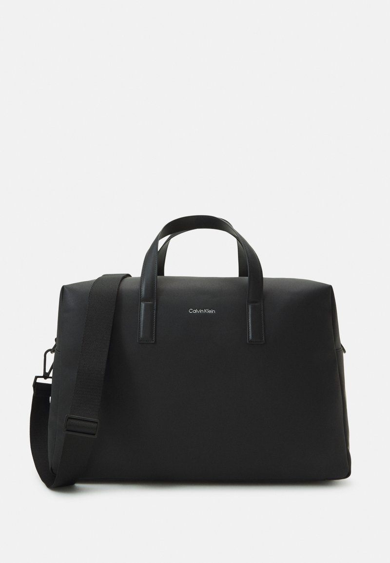 Borsa da viaggio nera con finitura liscia e opaca, doppio manico superiore e tracolla removibile. Presenta un logo del marchio discreto sulla parte anteriore.
