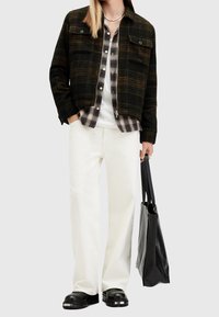 Károvaná flanelová košile vrstvená pod texturovanou černou bundou, bílé kalhoty s širokými nohavicemi a  černé boty, s černou kabelkou.