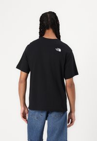 Camiseta de algodón negra con mangas cortas, con un logo blanco en la parte superior de la espalda. El corte es relajado, con un cuello redondo clásico.