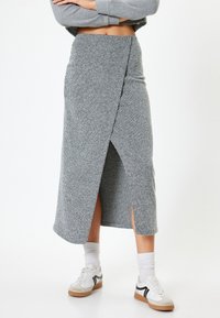 Gonna midi grigia a coste con design a portafoglio e spacchi laterali, abbinata a sneakers bianche e calze alla caviglia. Tessuto morbido e testurizzato.