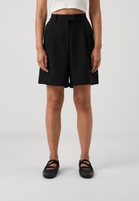 Svart skräddarsydda shorts med hög midja, slät front och sidofickor. Slät, lätt vikt tyg. Bärs med svarta sandaletter.
