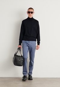 Suéter negro de cuello alto, pantalones azul claro, zapatos negros y gafas de sol. Lleva un bolso negro texturizado con un detalle de herrajes circular.