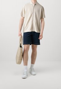 Beżowa dzianinowa koszulka z krótkim rękawem i geometrycznym wzorem, granatowe szorty, białe trampki oraz lekka pikowana torebka na ramię.