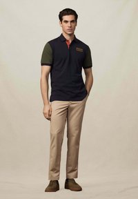 Námornícka polo košeľa so zelenými rukávmi a červeným golierom, s nášivkou loga. V kombinácii s béžovými nohavicami a hnedými teniskami. Hladký materiál.
