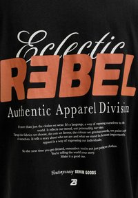 Black fabric with bold orange "REBEL" text overlaying white "Eclectic" and smaller white text about apparel expressing individuality and personal style.