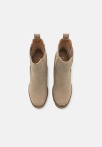 Une paire de bottines en suède beige avec des tirants, des panneaux latéraux élastiques et des semelles en caoutchouc marron, présentées vue de dessus sur un fond blanc.