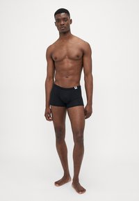 Schwarze Schwimmshorts aus leichtem Material, mit einer engen Passform und einem elastischen Bund, der vorne ein kleines Logoschild trägt.