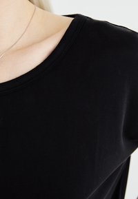 Black short-sleeve top with a round neckline, made of soft cotton. Features a smooth texture and subtle stitching along the edges.