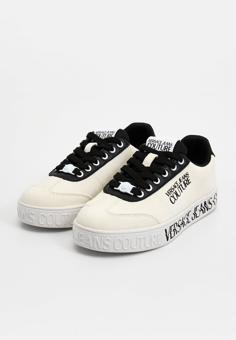 Zapatillas de ante beige con cordones negros, con detalles de logotipo blanco, suela blanca gruesa con texto en relieve "JEANS COUTURE" en el lateral.