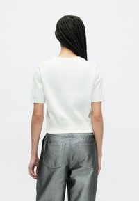 Weißes, kurzärmeliges Strickoberteil mit einem weiten, runden Ausschnitt und geripptem Saum, kombiniert mit silbernen Hosen mit Gesäßtaschen.