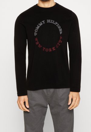 Camiseta negra de manga larga con escote redondo que presenta las palabras "TOMMY HILFIGER" y "NEW YORK CITY" en texto de contraste formando un patrón circular.