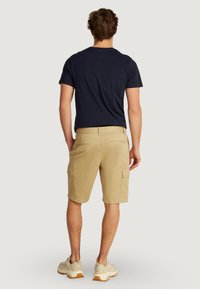 T-shirt à manches courtes bleu marine associé à un short cargo beige avec des poches latérales, une texture lisse et une coupe décontractée. Des baskets légères complètent le look.