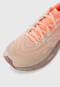 Light pink running shoe with orange accents, textured upper, gray highlights, and a distinct cushioned sole featuring the "FuelCell" branding.