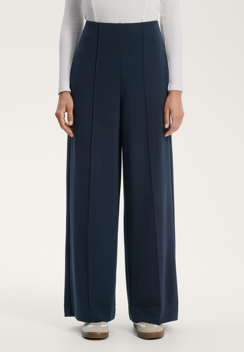 Mornarske široke hlače z visokim pasom, ki imajo sprednje gube in gladko teksturo. Ustavljene z svetlimi čevlji.