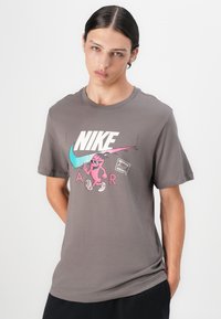 Šedé bavlněné tričko s velkým bílým logem "NIKE" na hrudi, s kreslenou postavičkou v růžových a tyrkysových akcentem.