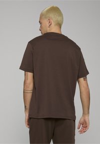 Hnědé bavlněné tričko s volným střihem, krátkými rukávy a kulatým výstřihem. Hladká textura, bez viditelných log nebo vzorů. Švy po stranách.