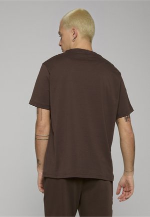 Ruskea puuvillainen t-paita, jossa rento istuvuus, lyhyet hihat ja pyöreä pääntie. Sileä pinta, ei näkyviä logoja tai kuvioita. Saumat sivuilla.