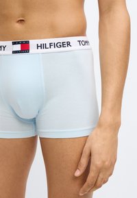 Ανοιχτό μπλε βαμβακερά ανδρικά εσώρουχα μποξέρ με λευκή μέση που έχει κόκκινες και ναυτικές λεπτομέρειες και το "TOMMY HILFIGER" τυπωμένο σε μαύρο.