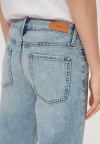 Jasnoniebieskie dżinsy z denimu z brązową skórzaną łatą z logo, wąski krój i dwie tylne kieszenie z widocznymi detalami przeszycia.