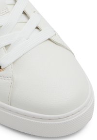 Close-up of white leather sneaker toe with textured rubber sole and white flat laces tied over eyelets.