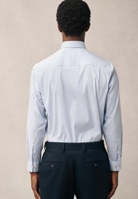 Chemise rayée bleu clair à manches longues et poignets boutonnés, assortie à un pantalon noir ajusté avec poches et boutons décoratifs.
