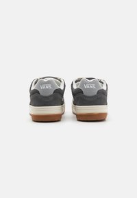 Baskets en suede gris avec des accents gris clair, semelles intermédiaires crème et semelles extérieures en caoutchouc gum. Présente un col rembourré et le logo Vans au dos.
