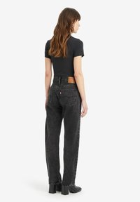 Hoge taille zwarte jeans in vervaagd denim, met een rechte pijp, zichtbare stiksels en een leren label aan de achterkant. De schoenen hebben blokhakken.