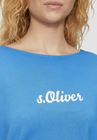 Blauwe top met korte mouwen, gemaakt van zachte katoen, met een wit s.Oliver-logo aan de voorkant. Gladde textuur met een brede halslijn.