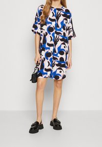 Vestido de manga corta en rosa, azul y negro con patrones abstractos. Presenta un corte recto y un ajuste relajado. Combinado con mocasines negros de suela gruesa.