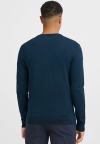 Námornícky modrý pletený sveter s okrúhlym výstrihom a dlhými rukávmi, s rebrovaným lemom a manžetami, zobrazený zozadu.