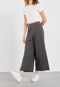 Pantalon gris à jambes larges en tissu texturé avec de subtiles rayures verticales, associé à un t-shirt court blanc et des baskets blanches.