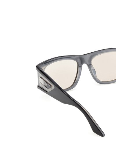 Lunettes de soleil grises avec une forme angulaire unique, monture transparente et verres légèrement teintés. Elles comportent un accent métallique sur le côté.