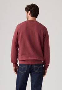 Bordeaux fleece sweatshirt met ronde halslijn en geribbelde manchetten, gecombineerd met donkerblauwe jeans met klassieke stiksels en achterzakken.