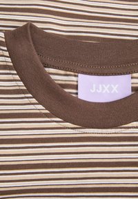 T-shirt rayé marron et crème avec un col rond côtelé, arborant une étiquette violet clair avec le texte "JJXX". Texture de tissu douce.