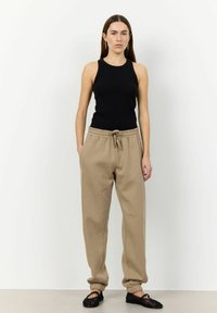 Schwarzes, tailliertes Tanktop kombiniert mit beigen Sweatpants mit Kordelzug, tapered Cuffs und seitlichen Taschen; schwarze gewebte Slipper.