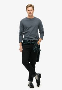 Grijze langemouwen shirt, zwarte jeans, groen geruit shirt om de taille geknoopt, grijze sokken en zwarte schoenen. Eenvoudig ontwerp en casual uitstraling.