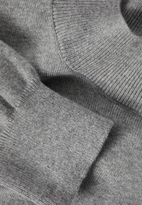 Tissu tricoté gris avec une finition douce et texturée. L'image met en évidence la surface lisse et les poignets côtelés.