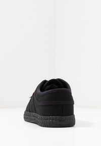 Baskets en toile noires avec une semelle en caoutchouc noir texturé. Présentent un design basse coupe et un look minimaliste, avec une languette à l'arrière pour un enfilage facile.